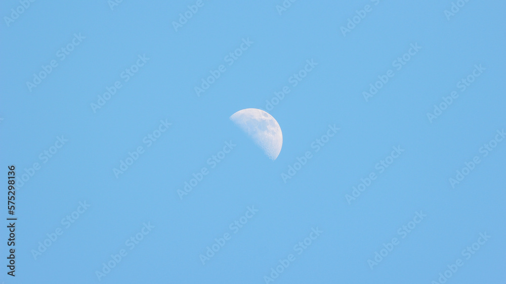 A crescent moon in the blue sky during the day.