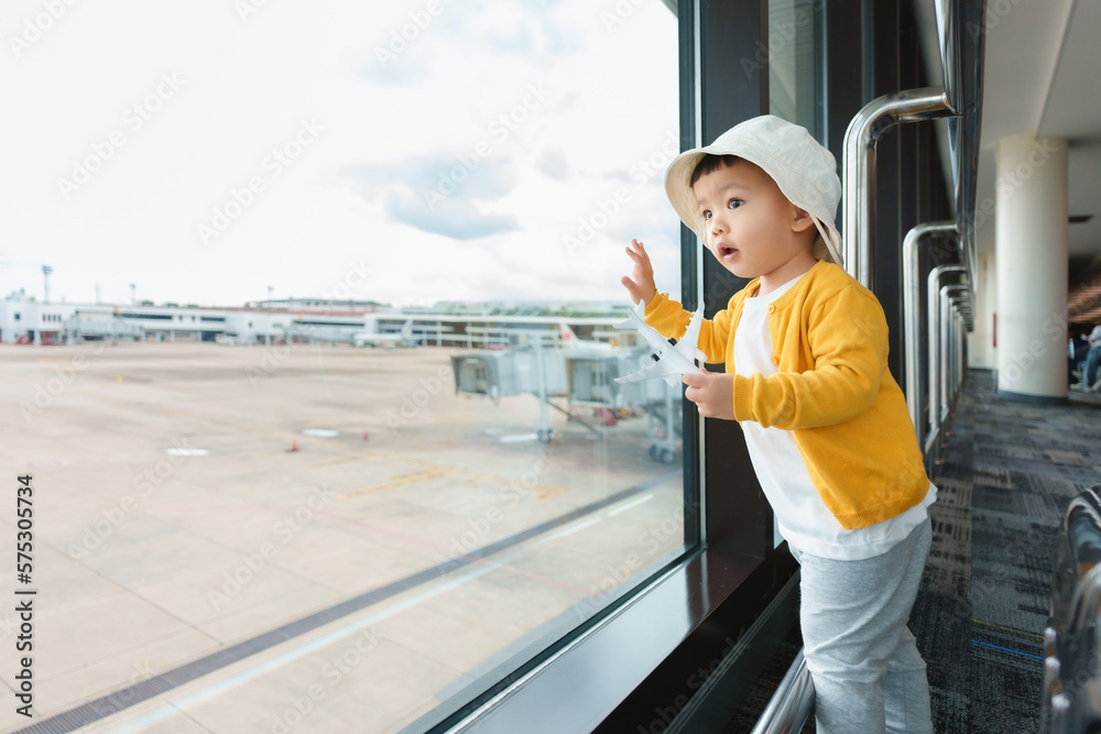 Obraz premium Asian Japanese Little child boy looking through window for airplane at international airport. Traveling.