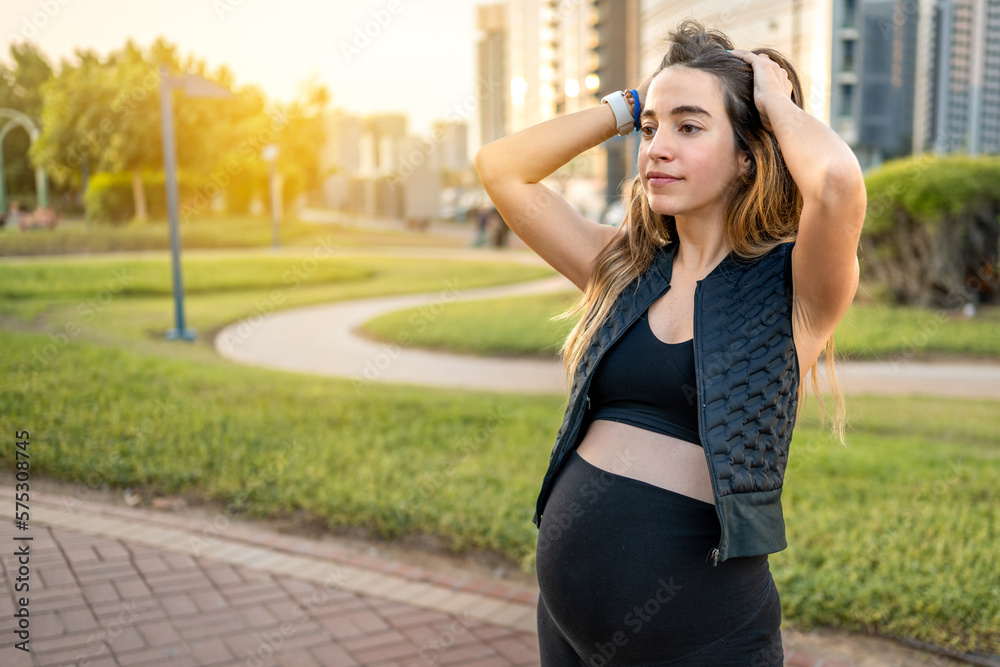 Portrait of beautiful young pregnant woman with hands on head enjoying calm sunset in the park.