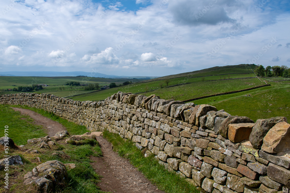 A section of Hadrian's Wall close to Milecastle 39 (Roman military base) and adjacent to a footpath route. in Northumberland National Park. With blue cloudy skies during summer 2022