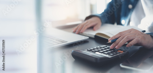 Business woman calculating monthly expenses, managing budget. Woman sitting at table using calculator to calculate tax refund, working at office with laptop computer on table, close up