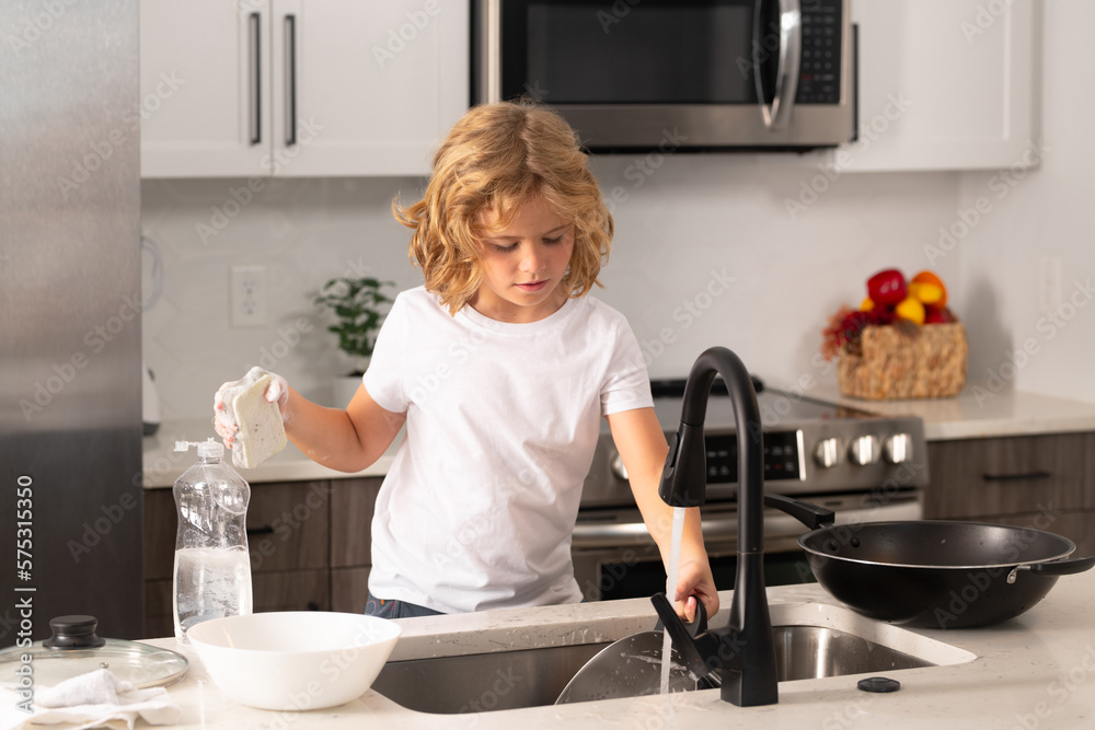 A little cute boy washing dishes near sink in kitchen. Clean washed dishes, dishwashing liquid with foam. A little cute boy washing dishes near sink in kitchen. Clean washed dishes, dishwashing liquid with foam.
