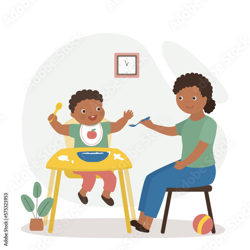 African american mother or nanny feeding small child. Childhood, child care, healthy nutrition. Happy boy eats delicious and healthy food. Calm mom holds spoon with food.