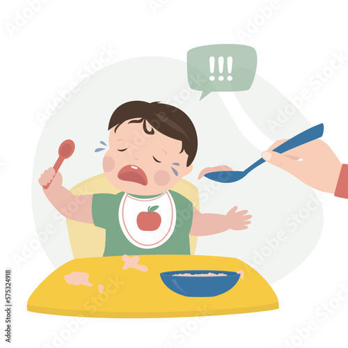 Mother or nanny trying to feed small child. The baby is crying and refuses to eat. Childhood, child care, difficulties and problems in raising young children. Hand holds spoon with food.