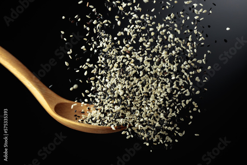 Grains of white and black sesame are poured with a wooden spoon.
