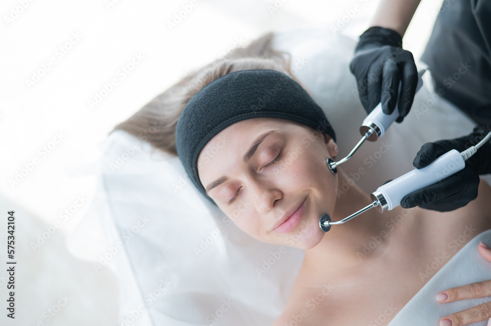 Naklejka premium Young caucasian woman on microcurrent therapy procedure. Beautician's office.