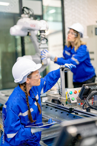 Two professional engineers or technician worker women help to check and maintenance robotic arm machine in factory workplace with quality control system.