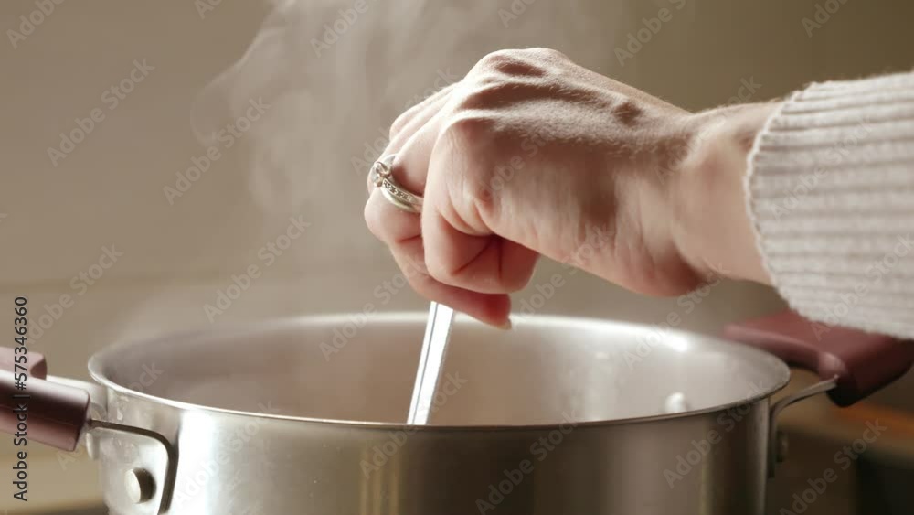 Closeup of female hand stirring soup with spoon. Healthy nutrition, cooking at home, hot steam Closeup of female hand stirring soup with spoon. Healthy nutrition, cooking at home, hot steam