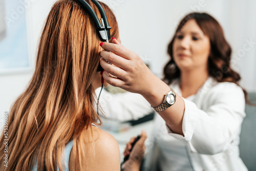 Audiologist doing impedance audiometry or diagnosis of hearing impairment. An beautiful redhead adult woman getting an auditory test at a hearing clinic.