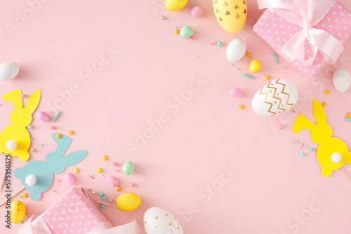 Easter concept. Flat lay photo of colorful eggs gift boxes cute paper bunnies and sprinkles on isolated pastel pink background with copyspace. Holiday card idea