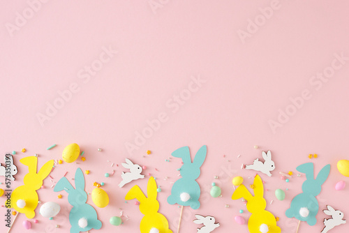 Easter decor concept. Top view photo of yellow white eggs cute rabbits paper bunny toppers and sprinkles on pastel pink background with emty space © Goncharuk film