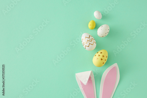 Easter concept. Top view photo of easter bunny ears yellow white eggs on isolated teal background with copy space. Holiday card idea
