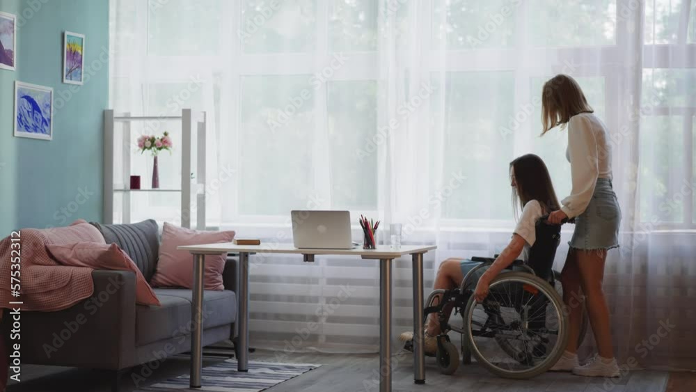 Young woman helps disabled sister in wheelchair get to table Young woman helps disabled sister in wheelchair get to table