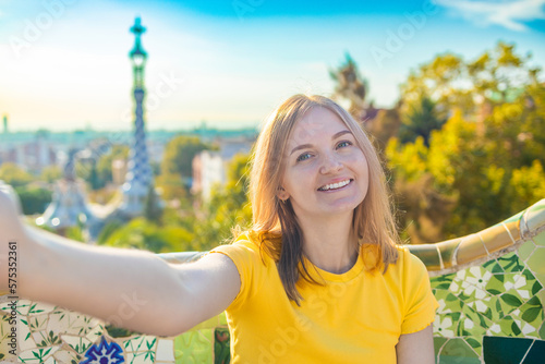 Photography Beautiful young woman looking at camera taking photo with smart phone smiling in Park Guell, Barcelona, Spain