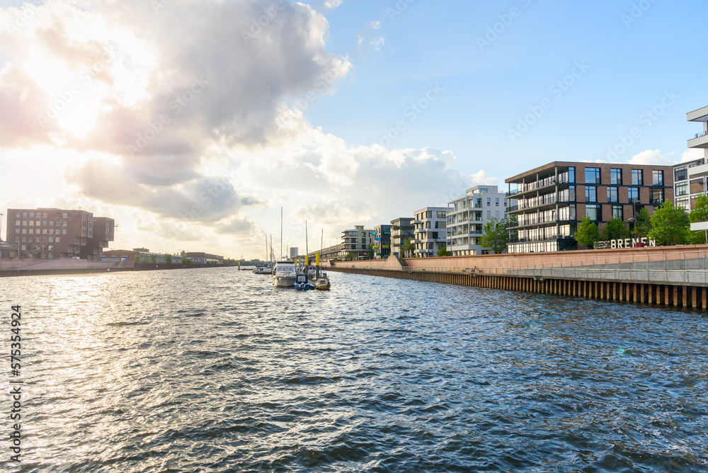Modern apartment buildings in a redevelopped area along a former river harbour at sunset. Boats moored to a jetty are visible in the middle of the harbour.
