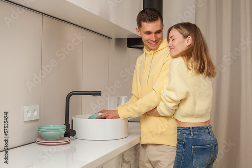 Happy man and woman in yellow clothes washing the dishes in the kitchen