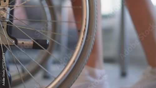 Legs of young nurse pushing wheelchair with large wheels in hospital. Woman takes care of patient with disability helping to move closeup