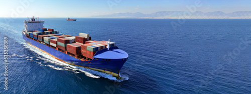 Aerial drone ultra wide panoramic photo of container tanker ship carrying truck size colourful containers in deep blue open ocean sea