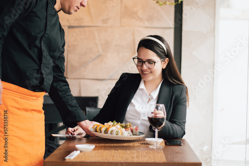 Smiling Latin woman receiving her order at a restaurant. : Executive woman receiving a plate of sushi from the waiter.