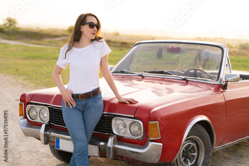 beautiful girl in retro style posing near vintage red cabriolet car.
