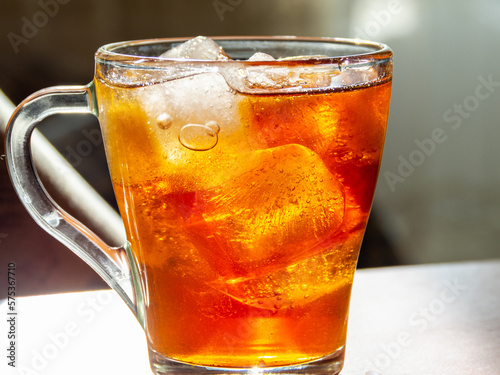 a glass of ice tea sitting on top of a table, window on background