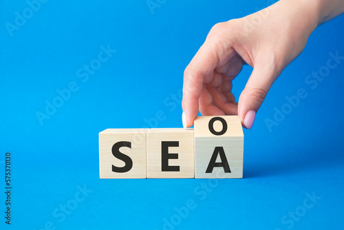 SEO vs SEA symbol. Businessman hand Turnes cube and changes word SEA to SEO. Beautiful blue background. Business and SEO vs SEA concept. Copy space