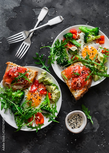 Delicious healthy breakfast - egg with vegetables, arugula salad and salmon cottage cheese toast on a dark background, top view