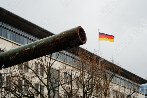Rusty barrel of a tank gun aiming at the German flag on top of a building