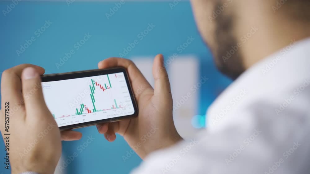 Male hands holding phone checking stock market chart for trading and investing in crypto exchange. Male hands holding phone checking stock market chart for trading and investing in crypto exchange.