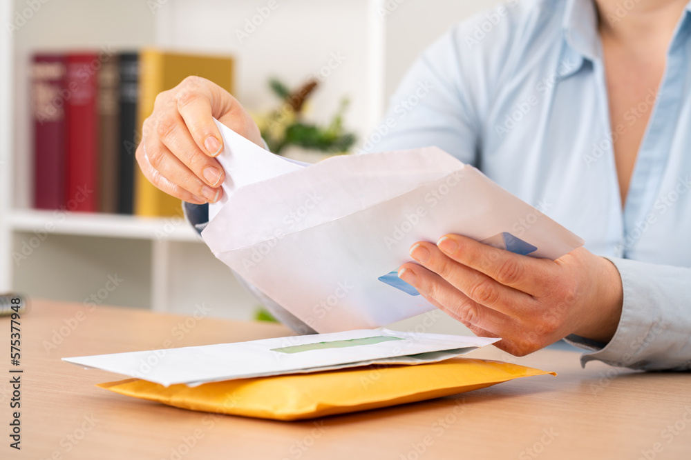 Close up of woman hands putting a letter inside an envelope on a desk at home or office - obrazy, fototapety, plakaty 