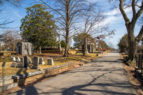 A gorgeous winter landscape in the graveyard with headstones, graves, bare winter trees, lush green trees, plants and flowers at the Oakland Cemetery with a blue sky and clouds in Atlanta Georgia USA photo