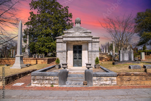 a large stone mausoleum in the graveyard  with bare winter trees and lush green trees and powerful cloudsat sunset at the Oakland Cemetery in Atlanta Georgia USA photo