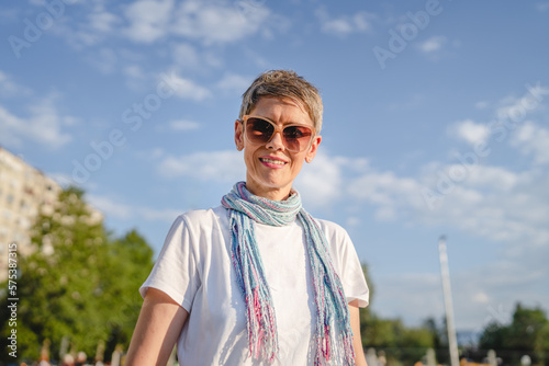 One mature woman caucasian female standing outdoor in sunny summer day wearing eyeglasses with short gray hair happy smile confident looking to the camera in parking lot copy space white t-shirt
