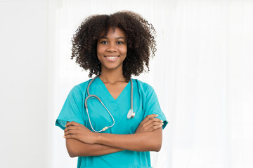 Portrait of smiling young female doctor or young nurse wearing blue scrubs uniform and stethoscope and standing with arms crossed while looking at camera isolated on white background