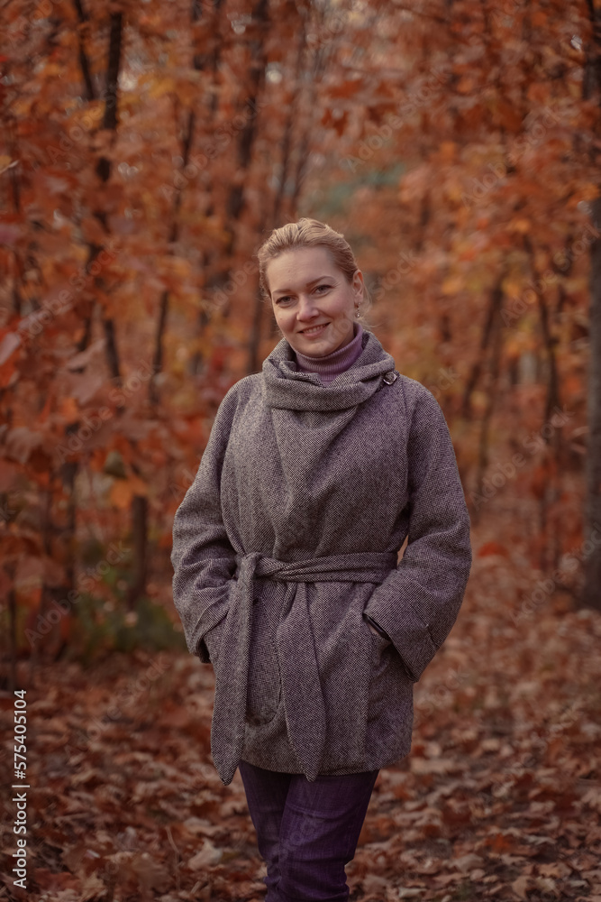 Beautiful smiling woman in a coat in the autumn forest. Brown toned.
