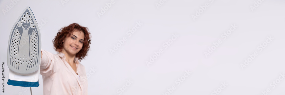 Panoramic frame. The girl holds the iron on her outstretched hand right in front of her. Panoramic frame. The girl holds the iron on her outstretched hand right in front of her.