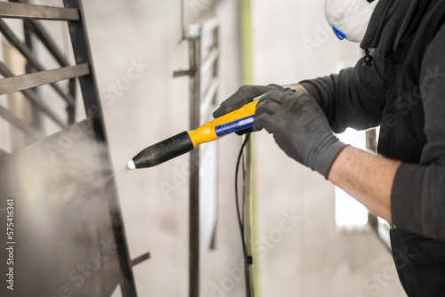 The detail of a man working in a factory finishes a job using the technique of electrostatic powder coating with a spray gun.