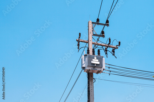 AC high-voltage power transformer on electric pole with wires on a background of blue sky, high voltage transmission line.