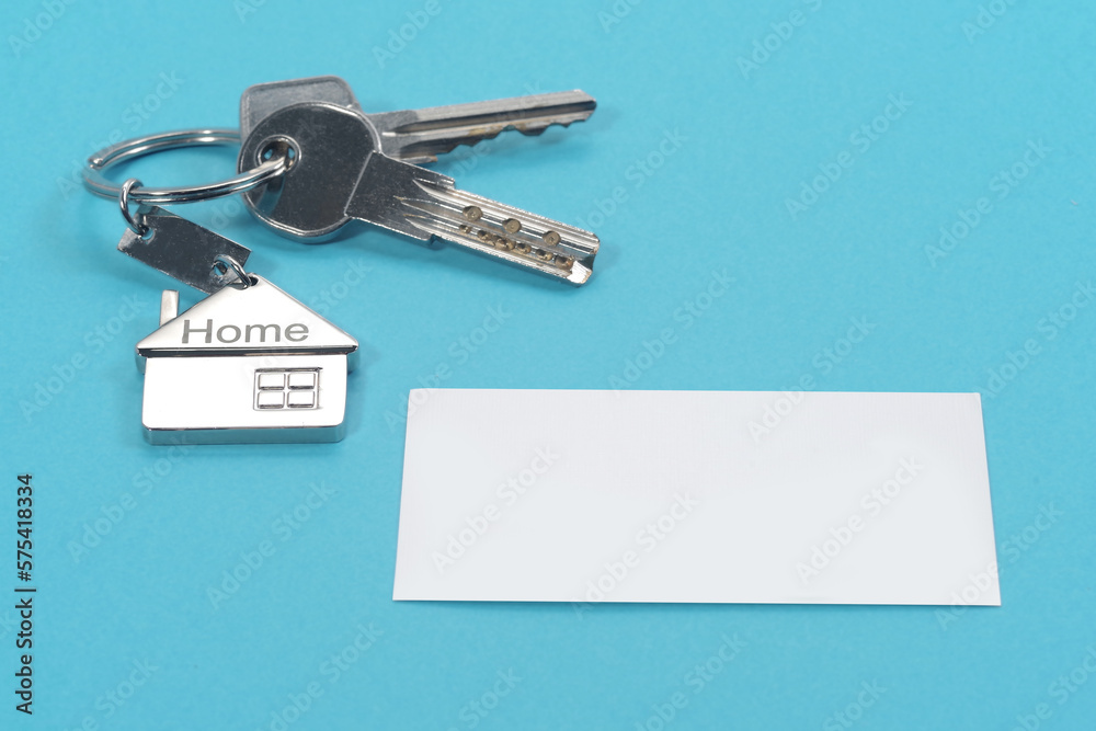 House symbol with silver keys and blank white business card on blue background. Real estate concept House symbol with silver keys and blank white business card on blue background. Real estate concept