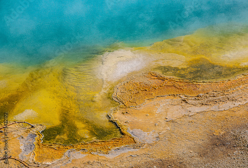 Abstract Colorful Underwater Minerals in Yellowstone Hot Pool. Depicts brown, yellow, rust, turquoise, blue and green colored minerals in a Yellowstone hot pool. Steam is rising from the pool. 