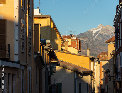 Chiaroscuro photography of houses in Gap, Hautes Alpes, France. Beautiful orange evening light and mountains covered with snow in the background.