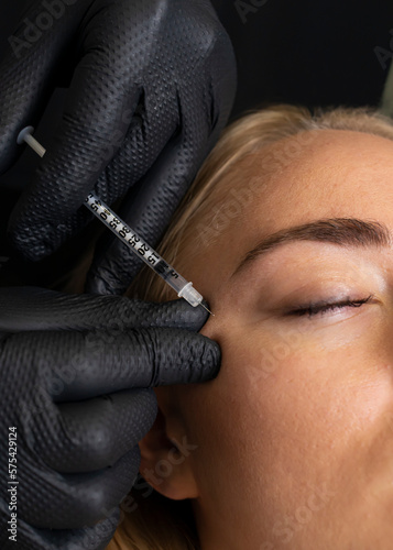 Closeup of Caucasian woman gets botox cosmetic injection in eye area. Beauty physician inserts needle of syringe into face of beautiful female. Cosmetologist, aesthetic medicine. Vertical
