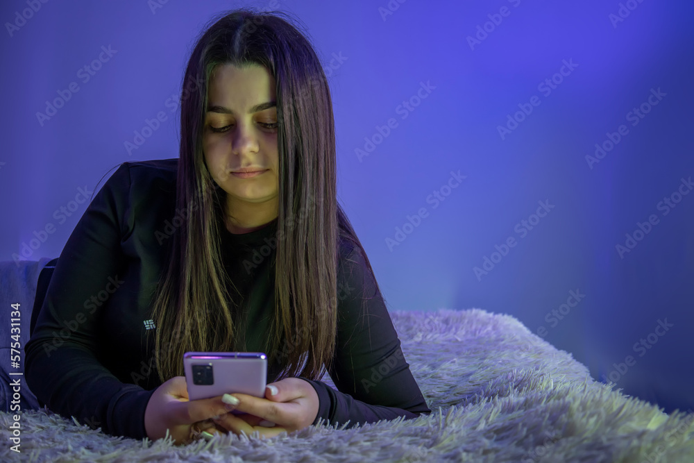 A beautiful young girl is lying on the bed with a mobile phone A beautiful young girl is lying on the bed with a mobile phone