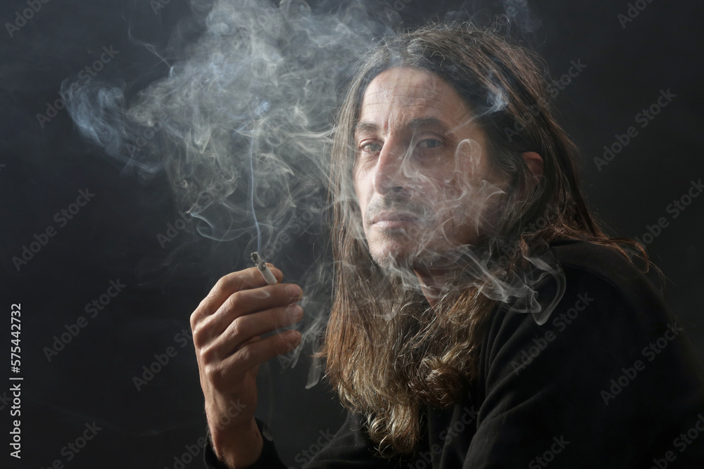 Studio portrait on black background of middle age man with long hair smoking cigarette Studio portrait on black background of middle age man with long hair smoking cigarette
