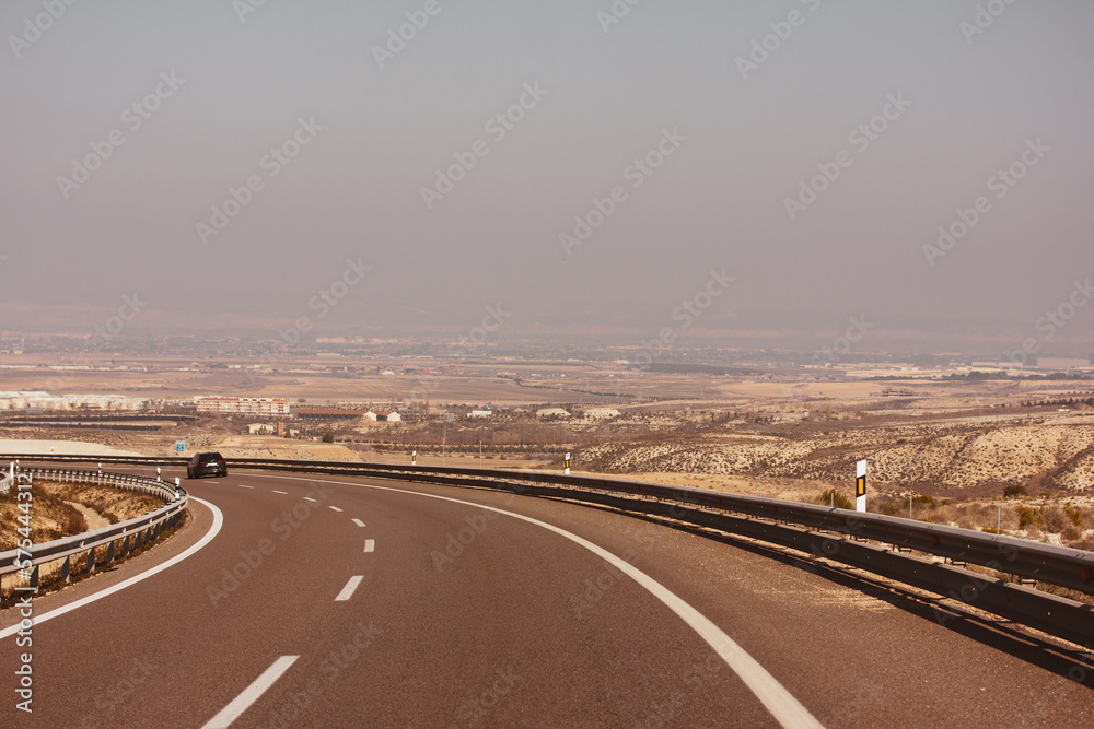 Fototapeta premium Curve road in a desert dry landscape. A bend of an asphalt road with excellent pavement, a dividing strip and a guardrail. Infrastructure, mobility, movement concept. Travel around the world, car trip