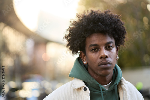 Cool sad lonely young African American guy standing at city street. Stylish serious pensive sensitive vulnerable ethnic rebel hipster gen z teen boy looking at camera outdoors, close up portrait.