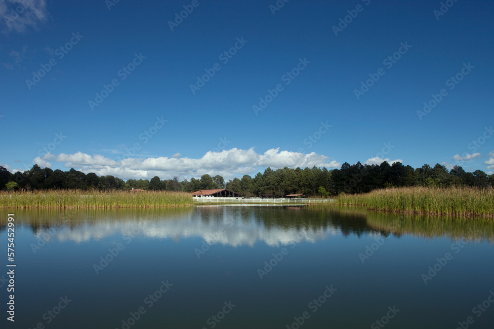 Vista de un rancho reflejado en el lago con un bosque al fondo