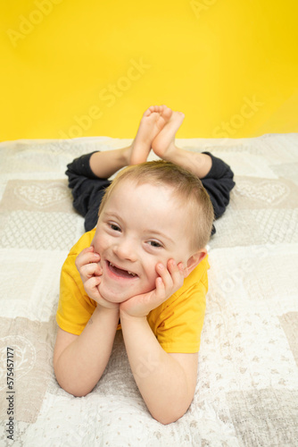 Cute boy with Down syndrome is lying in bed and smiling. People with disabilities inclusion, awareness and support. Family, love, happiness.