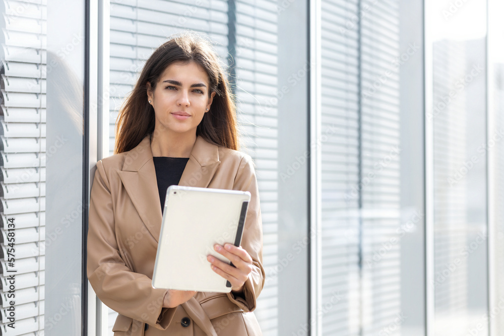 Smiling successful young business woman in stylish business attire holding digital tablet computer looks at the camera, success concept Smiling successful young business woman in stylish business attire holding digital tablet computer looks at the camera, success concept