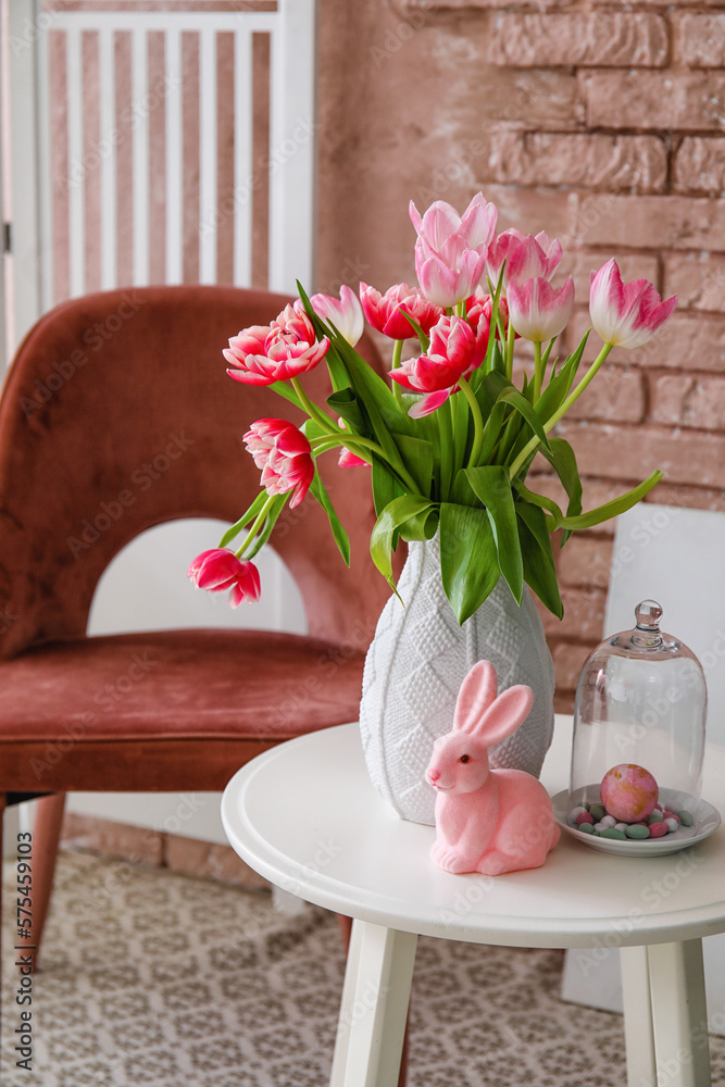 Vase with tulips and Easter bunny on end table and armchair near brick wall